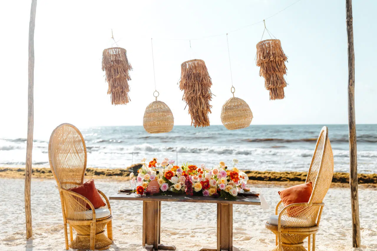 Sweetheart table with rattan chairs and florals on the sand