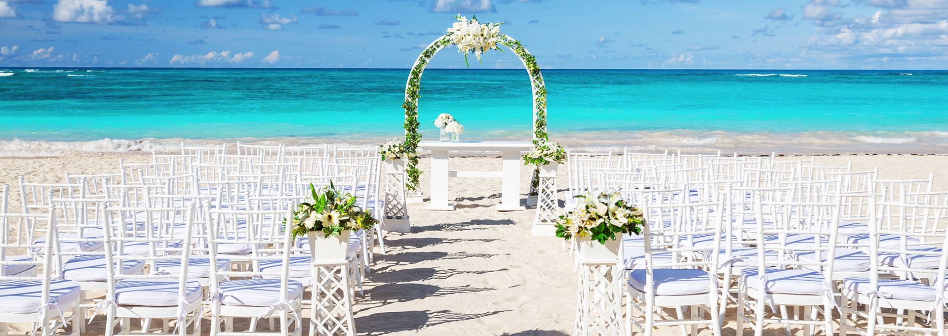 White beach wedding ceremony with floral arch overlooking the turquoise Caribbean